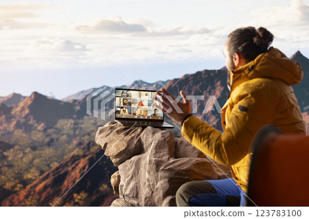 Adventure seeker employee meeting with workmates on video call, enjoying strong signal at internet on top of the mountain. Male explorer entrepreneur with technology dependency. 123783100
