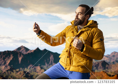 Nature lover takes pictures of himself standing on a mountain top, absorbing the beauty of the wilderness. High altitude adventure symbolizes resilience and personal growth, photography. 123783105