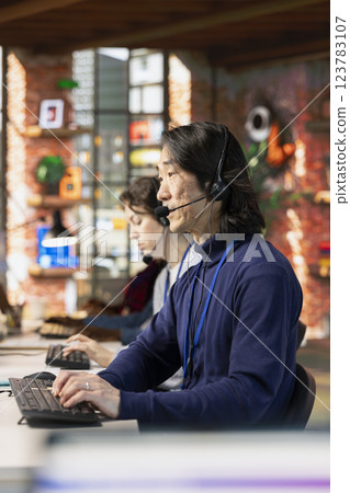 Call center agent in office helping customers by answering questions, solving their issue. Man in customer support workspace in front of PC using headset mic to talk with clients 123783107