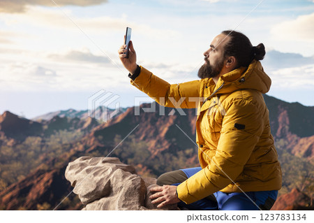 Hiker adventure seeker captures the breathtaking scenic view at the top of mountain, gazes at a distant mountain range and embraces beauty of the wilderness. Joy of discovering wonders. 123783134