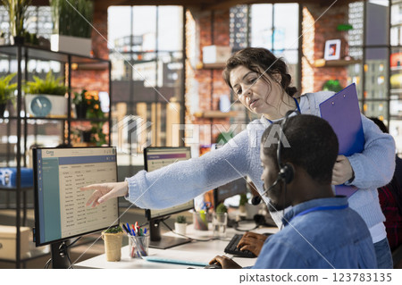 Customer center manager teaching man how to log customer interactions in CSM system on computer. Call center onboarding specialist tutoring intern on using customer service management software 123783135