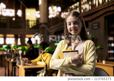 Portrait of clever caucasian scholar posing with her textbooks in the library, feeling ambitious to finish school with perfect grades. Teenage girl preparing for her exams, academic focus. 123783173
