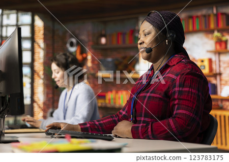 Call center employee using audio headset to answer customers technical inquiries about software issues. African american woman doing customer service job using PC to troubleshoot problems Call center employee using audio headset to answer customers technical inquiries about software issues. African american woman doing customer service job using PC to troubleshoot problems 123783175