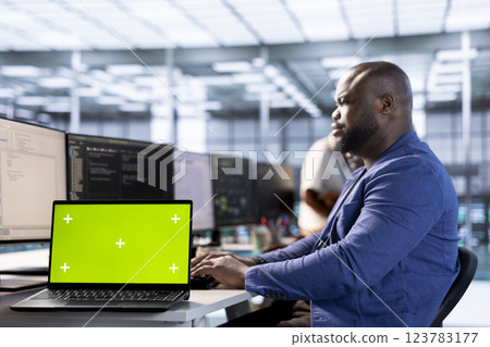 Server room programmer using green screen laptop to find firewall misconfigurations. African american man checking systems bottlenecks leading to sluggish data transfer rates using mockup notebook 123783177