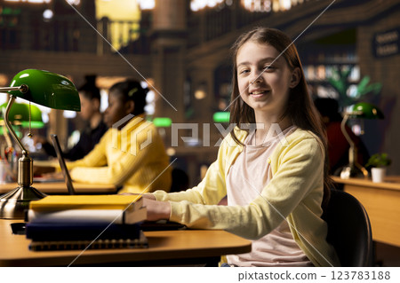 Portrait of a cute schoolgirl working on a project in the school library, using the academic database for homework research. Preteen student solving her school assignments for higher grades. 123783188