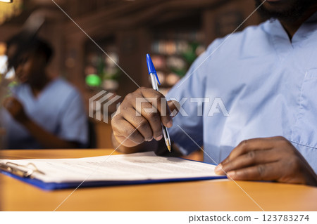 African american student takes notes about medical practice to prepare for an exam, studying to obtain his med school diploma and build a career in healthcare. Scholar writes data. Close up. 123783274
