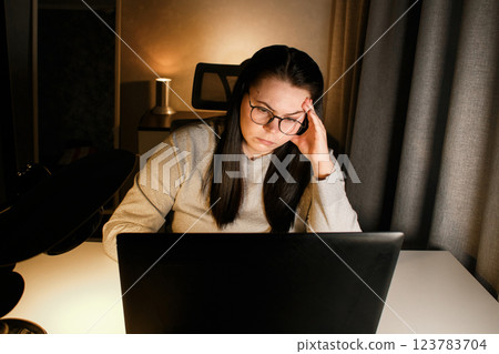 Young woman with eyeglasses working on laptop at home late at night, using modern technologies and getting online education. Remote learning concept. Online university. Focus on process. Young woman with eyeglasses working on laptop at home late at night, using modern technologies and getting online education. Remote learning concept. Online university. Focus on process. 123783704