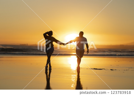 Couple walking on beach at sunset holding hands Couple walking on beach at sunset holding hands 123783918