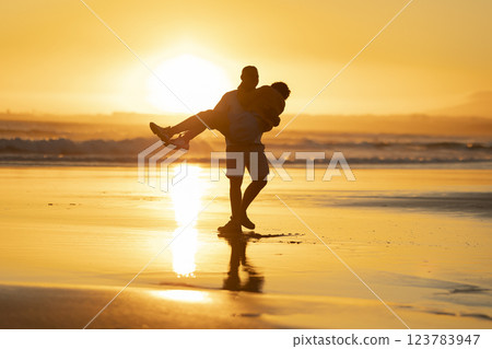 Couple walking on beach at sunset, man carrying woman in his arms 123783947