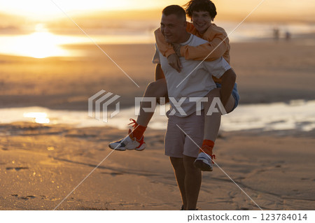 Happy couple piggybacking on beach at sunset Happy couple piggybacking on beach at sunset 123784014