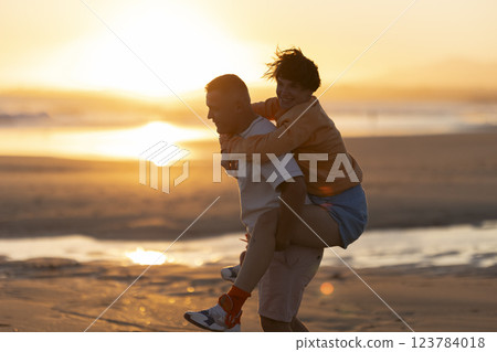 Happy couple piggybacking on beach at sunset Happy couple piggybacking on beach at sunset 123784018