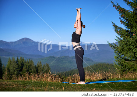 Woman practicing yoga outdoors in the mountains in a serene, natural setting. Female performing yoga pose on mat, with backdrop of beautiful mountain landscape at sunrise or sunset. Woman practicing yoga outdoors in the mountains in a serene, natural setting. Female performing yoga pose on mat, with backdrop of beautiful mountain landscape at sunrise or sunset. 123784488