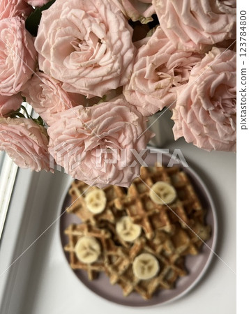 beautiful bouquet of light pink roses on the windowsill with freshly baked homemade waffles decorated with banana breakfast 123784800