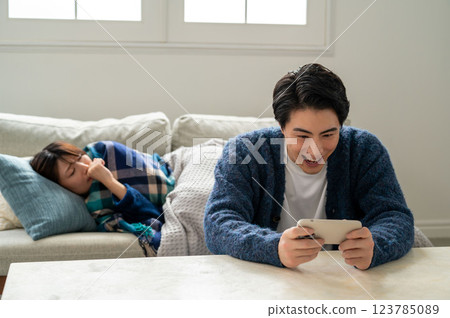 A man who is too absorbed in his smartphone to take care of his sick wife A man who is too absorbed in his smartphone to take care of his sick wife 123785089