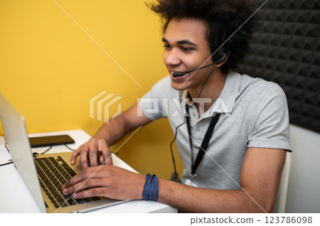 Young man sitting at the laptop and talking to the client online Young man sitting at the laptop and talking to the client online 123786098