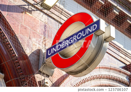 The iconic red and blue sign marks an entrance to the London Underground in England. It is surrounded by historical architecture, highlighting the city's vibrant transit system. 123786107