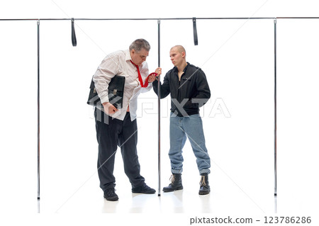 Businessman with loosened tie facing intense stare from younger man in casual attire against white background. Concept of city lifestyle Businessman with loosened tie facing intense stare from younger man in casual attire against white background. Concept of city lifestyle 123786286