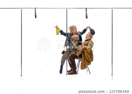 Woman teasing elderly man while holding bottle, pulling his cap against white studio background. Woman teasing elderly man while holding bottle, pulling his cap against white studio background. 123786349