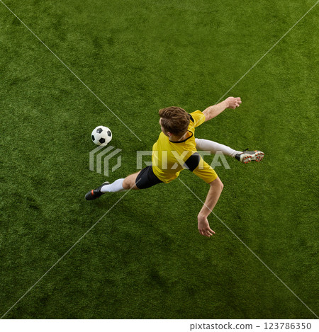 Top view dynamic image of determined young man, soccer player in motion on green stadium, controlling ball, playing. 123786350