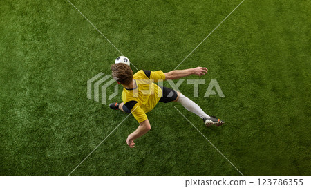 Top view image of young man, soccer player in yellow jersey playing,m dribbling ball on green stadium field, training 123786355