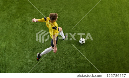 Top view image of young man, soccer player in yellow jersey playing,m dribbling ball on green stadium field, training Top view image of young man, soccer player in yellow jersey playing,m dribbling ball on green stadium field, training 123786357