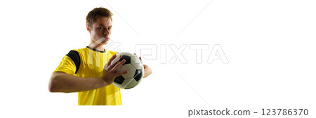 Side view of focused and determined man, soccer player in yellow jersey standing with ball and looking at camera with intense gaze. Champion Side view of focused and determined man, soccer player in yellow jersey standing with ball and looking at camera with intense gaze. Champion 123786370
