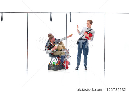 Young man, student rejecting food from homeless man sitting with cardboard box and bottles against white studio background. Young man, student rejecting food from homeless man sitting with cardboard box and bottles against white studio background. 123786382