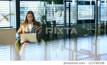 Businesswoman typing on laptop in modern office, surrounded by reflections from glass walls. Businesswoman typing on laptop in modern office, surrounded by reflections from glass walls. 123786386