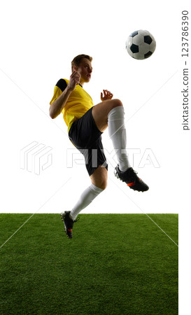 Dynamic image of man, soccer player in yellow jersey and black shorts, kicking ball with knee, training against white background. Dynamic image of man, soccer player in yellow jersey and black shorts, kicking ball with knee, training against white background. 123786390