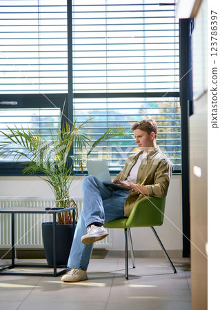 Young entrepreneur in casual attire working on laptop in relaxed office setting with minimalistic design. 123786397