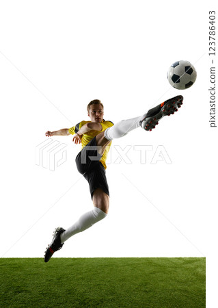 Low angle view of young man, soccer player kicking ball in motion in a jump, with outstretched leg against white background. 123786403