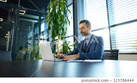 Confident businessman typing on laptop, making important business decisions in professional workspace. Confident businessman typing on laptop, making important business decisions in professional workspace. 123786444