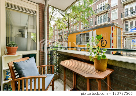 A charming balcony setup featuring a small table, a comfortable chair, and green plants against a backdrop of urban architecture. Perfect for relaxation. 123787505