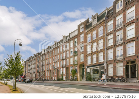 A picturesque view of a charming Amsterdam street lined with historic brick buildings, bicycles, and serene blue skies. The atmosphere reflects the city's unique architecture. A picturesque view of a charming Amsterdam street lined with historic brick buildings, bicycles, and serene blue skies. The atmosphere reflects the city's unique architecture. 123787516
