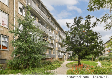 A modern residential building features balconies and is surrounded by lush greenery and well-maintained garden areas, creating a peaceful urban oasis. A modern residential building features balconies and is surrounded by lush greenery and well-maintained garden areas, creating a peaceful urban oasis. 123787519