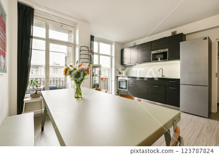 A contemporary kitchen featuring sleek cabinets, a dining table, and a vase of fresh flowers adding a touch of elegance to the space. A contemporary kitchen featuring sleek cabinets, a dining table, and a vase of fresh flowers adding a touch of elegance to the space. 123787824