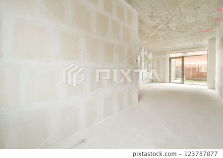 A spacious interior in the process of construction, featuring bare walls and a concrete ceiling. Natural light filters through an opening, highlighting the unfinished space. A spacious interior in the process of construction, featuring bare walls and a concrete ceiling. Natural light filters through an opening, highlighting the unfinished space. 123787877