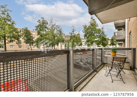 A contemporary balcony view featuring green trees lining the street, along with a simple table and chair setup, creating a serene outdoor space. 123787956