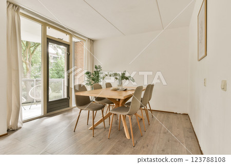 A stylish dining area featuring a wooden table and gray chairs, bathed in soft natural light from large windows with a serene outdoor view. 123788108