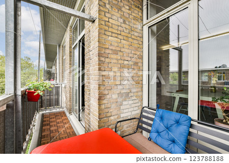 A stylish modern balcony showcasing red furniture, green plants, and large windows that enhance the aesthetic of urban living. Perfect for relaxation and outdoor enjoyment. 123788188