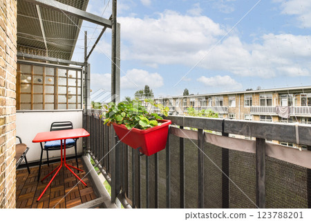 A bright, inviting balcony featuring a small red table and chair, adorned with potted plants, creating a serene outdoor space for relaxation. A bright, inviting balcony featuring a small red table and chair, adorned with potted plants, creating a serene outdoor space for relaxation. 123788201