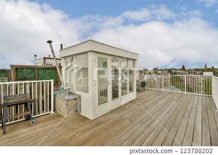 Stylish rooftop deck featuring wooden flooring, a grill station, and panoramic views of the city skyline under a partly cloudy sky. 123788202