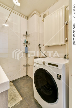 A clean and contemporary laundry space featuring a washing machine, shelves, and modern fixtures. The design emphasizes functionality and minimalist aesthetics. 123788322