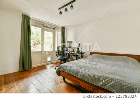 A stylish, modern bedroom featuring wooden flooring, a comfortable bed, and large windows with green curtains that invite natural light. 123788324