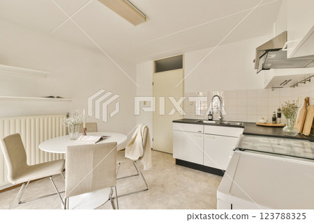 Contemporary kitchen showcasing a minimalist design with clean lines, light colors, and functional furnishings, ideal for cozy cooking spaces. 123788325