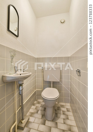A compact bathroom featuring a white toilet and a small sink against a tiled wall, emphasizing simplicity and modernity in its design. 123788333