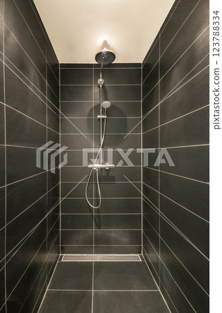 A sleek and elegant modern shower interior featuring dark tiles, clean lines, and a minimalist aesthetic. The design emphasizes simplicity and functionality. 123788334