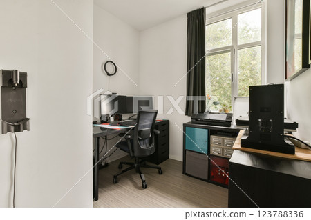 A stylish home office featuring a desk, computer setup, and natural light from a large window. Modern design elements enhance the workspace atmosphere. 123788336