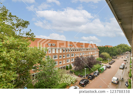 A picturesque view of a residential block adorned with lush greenery, accompanied by parked cars along a tree-lined street under a bright sky. 123788338