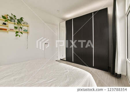 A sleek and contemporary bedroom interior featuring a light-colored bedspread, stylish wardrobe, and minimalist decor that emphasizes simplicity and comfort. A sleek and contemporary bedroom interior featuring a light-colored bedspread, stylish wardrobe, and minimalist decor that emphasizes simplicity and comfort. 123788354